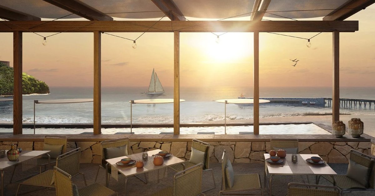 An open-air beachfront restaurant with ocean views, sunset lighting, and sailboat scenery beyond outdoor dining tables.