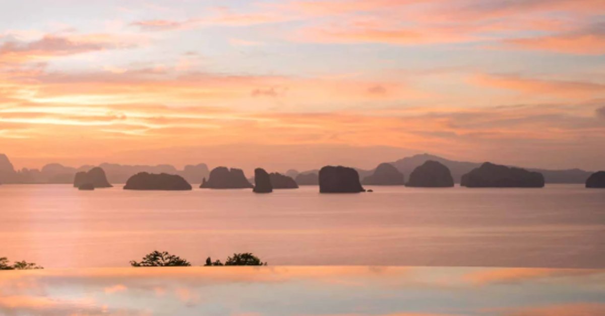 A calm ocean view at sunset with small islands, soft clouds, orange light, and reflections on the water.