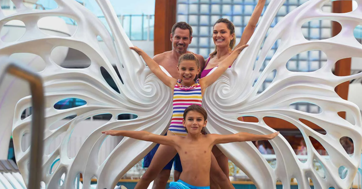 Family of four poses with large white butterfly wings beside a pool, with two children standing in front of their parents.